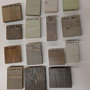 May include: A collection of 14 wood stain samples, each with a different color and name. The names include Vintage Olive, Sunwash Blue, Antique Jade, Watered Classic Black, Juniper Mist, Coastal Grey, River Stone, Classic Black, Special Walnut, Charcoal Grey, Classic Grey, Tin Smith Grey, Watered Onyx, and Onyx.