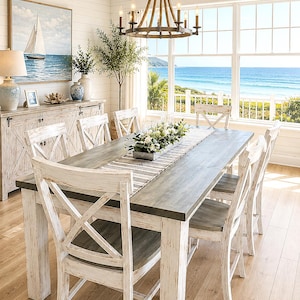 May include: A rectangular dining table with a gray wooden top and distressed white legs, surrounded by six matching chairs with X-back designs. A metal trough centerpiece filled with white flowers sits on a striped runner atop the table.