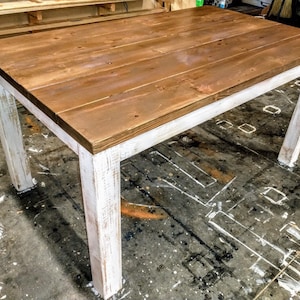 Puede incluir: Una mesa de madera r&uacute;stica con una base blanqueada. La superficie de la mesa est&aacute; hecha de tablones de madera natural y tiene un acabado te&ntilde;ido marr&oacute;n. Las patas de la mesa son blancas con un acabado desgastado.
