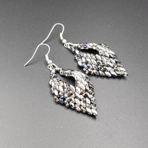 May include: A pair of silver dangle earrings with a teardrop shape. The earrings are made of small, iridescent beads that create a shimmering effect.