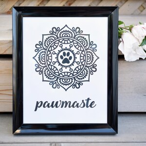 May include: Black and white framed print with a mandala design featuring a paw print in the centre. The text "pawmaste" is printed below the mandala.