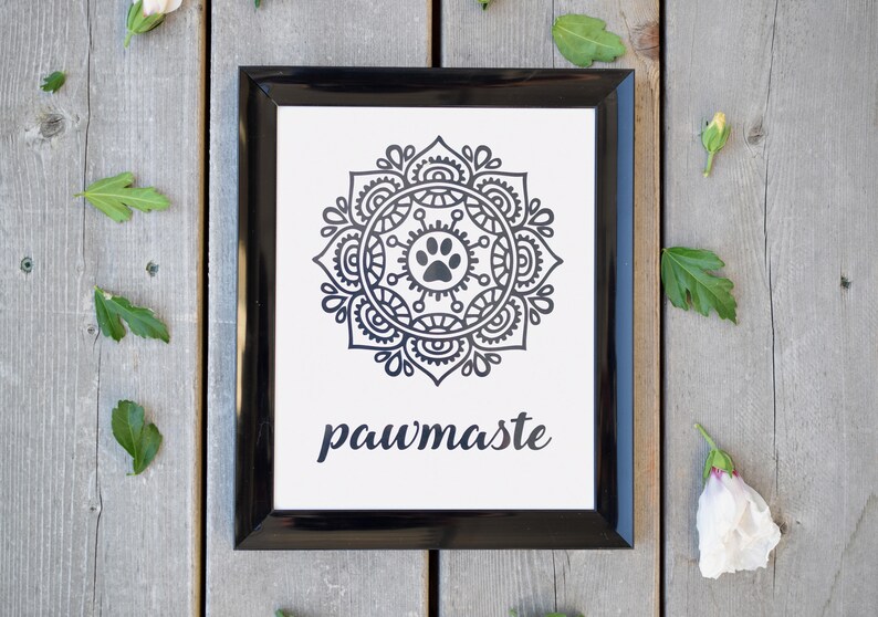 May include: Black and white framed print with a mandala design featuring a paw print in the centre. The text "pawmaste" is written below the mandala.