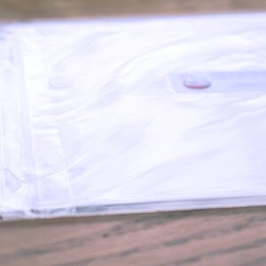 Puede incluir: Una bolsa de pl&aacute;stico blanca con una etiqueta roja y blanca. La bolsa est&aacute; doblada y apoyada sobre una superficie de madera.