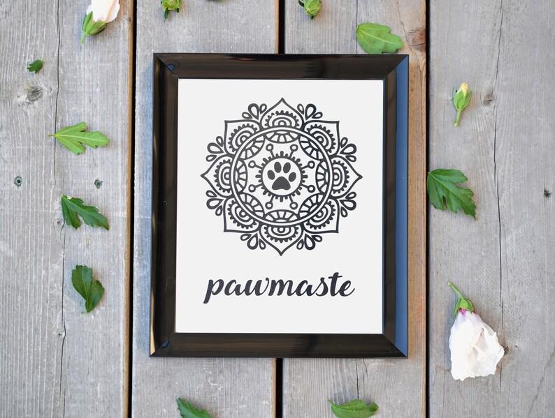 May include: Black and white print with a mandala design featuring a paw print in the centre. The print is framed in a black frame and has the text "pawmaste" below the mandala.