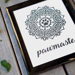 May include: Black and white framed print with a mandala design featuring a paw print in the centre. The text "pawmaste" is written below the mandala.