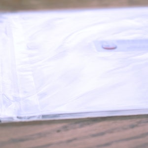 May include: A white plastic bag with a red label. The bag is folded and sealed.