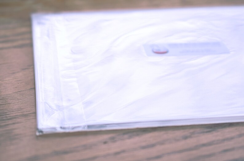 May include: A white plastic bag with a red label. The bag is folded and sealed.