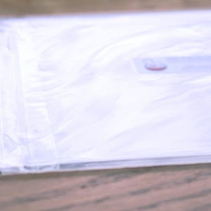 May include: A white plastic bag with a red and white label. The bag is folded and lying on a wooden surface.