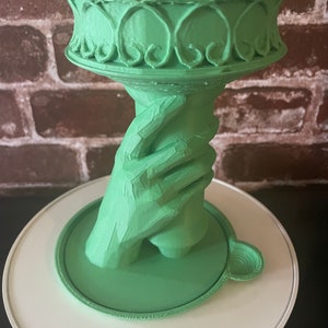 May include: A green 3D printed statue of the Statue of Liberty's hand holding a torch. The torch is a cup-shaped object.