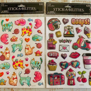 May include: Two sheets of colorful, puffy stickers. The left sheet features a variety of cats with different patterns and colors. The right sheet features a variety of stickers with a colorful, modern theme, including a scooter, sunglasses, a cupcake, and a gum ball machine. The text "STICK-A-BILITIES" is printed on both sheets.