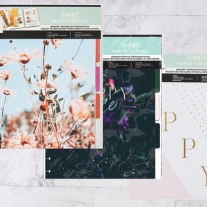 May include: Three Happy Planner Memory Keeping Extension Packs with different designs. The first pack features a floral design with pink and white flowers on a blue background. The second pack features a dark green and black floral design with purple flowers. The third pack features a white background with gold polka dots and the word "Happy" in gold letters.