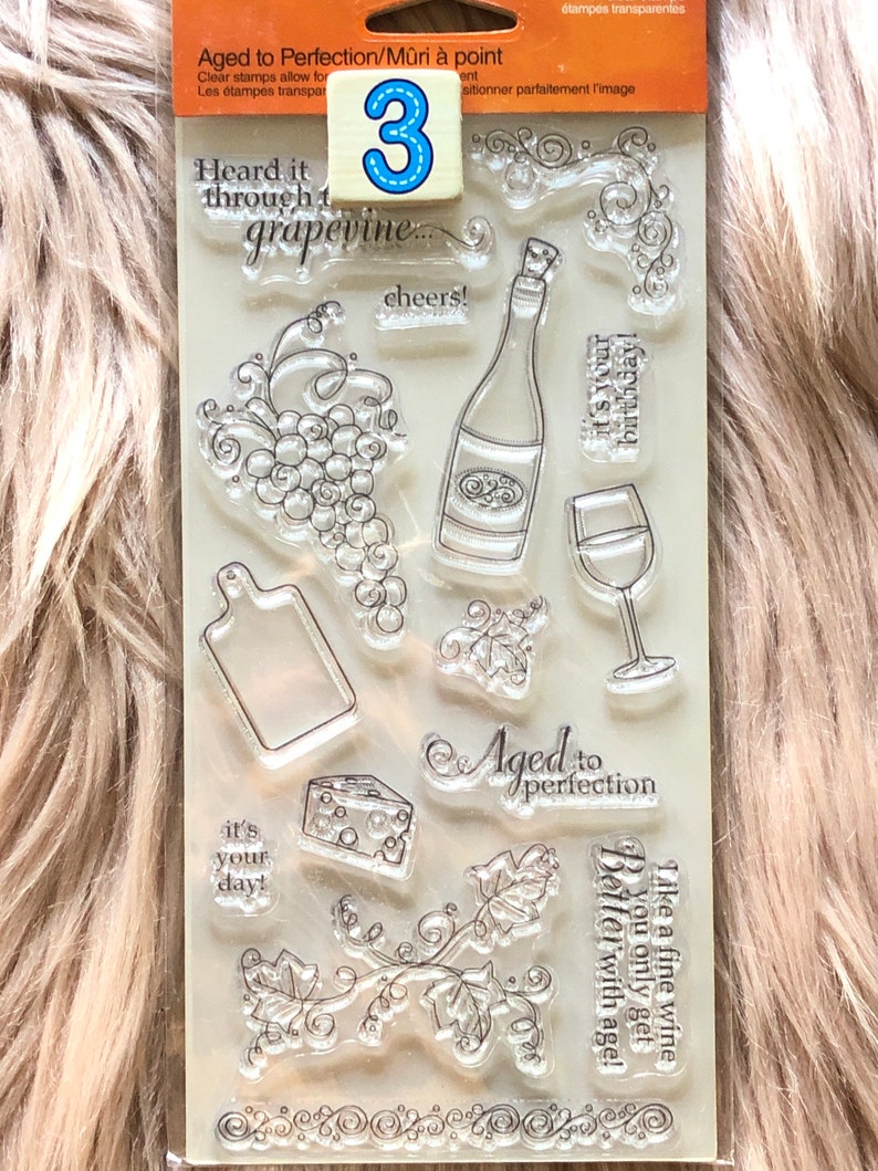 May include: A clear plastic sheet with 10 different rubber stamps for crafting. The stamps feature wine-themed images, including grapes, wine bottles, wine glasses, and the text "Aged to Perfection".