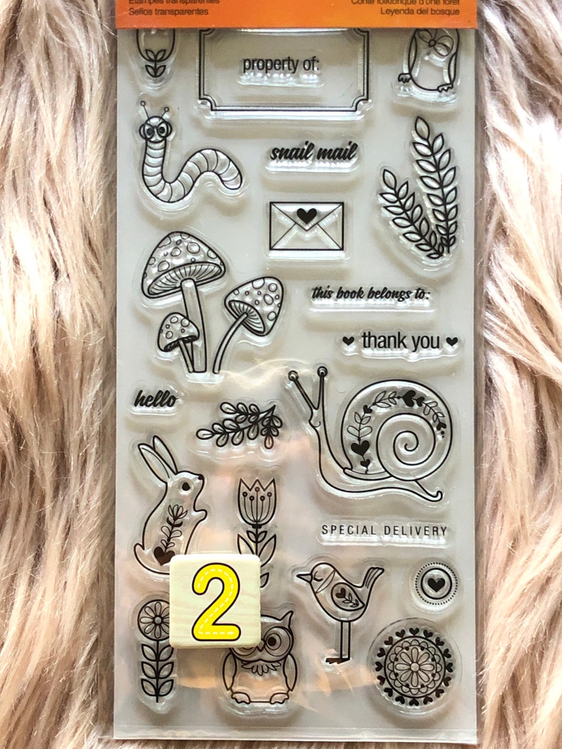 May include: A clear sheet of transparent stamps with various designs, including a snail, a bird, a mushroom, a flower, an owl, a bunny, and a caterpillar. The stamps are arranged in a grid pattern on a white background. The text "property of:", "snail mail", "this book belongs to:", "thank you", "hello", and "SPECIAL DELIVERY" are also included on the sheet.