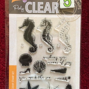 May include: A clear stamp set with five sea-themed images. The images include seahorses, seashells, starfish, and the text "wishing you oceans of joy" and "you, me & the sea".