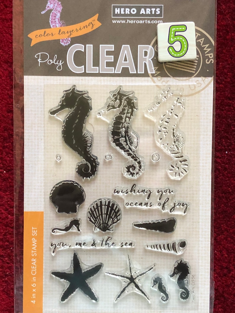 May include: A clear stamp set with five sea-themed images. The images include seahorses, seashells, starfish, and the text "wishing you oceans of joy" and "you, me & the sea".