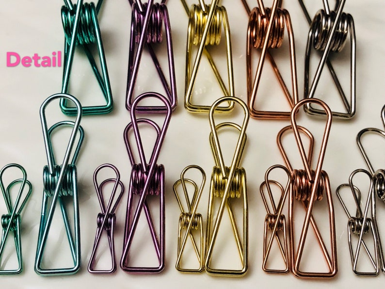 May include: Assortment of ten metal binder clips in various colors, including teal, purple, gold, copper, and silver. The clips are all the same size and shape, with a spring-loaded mechanism.