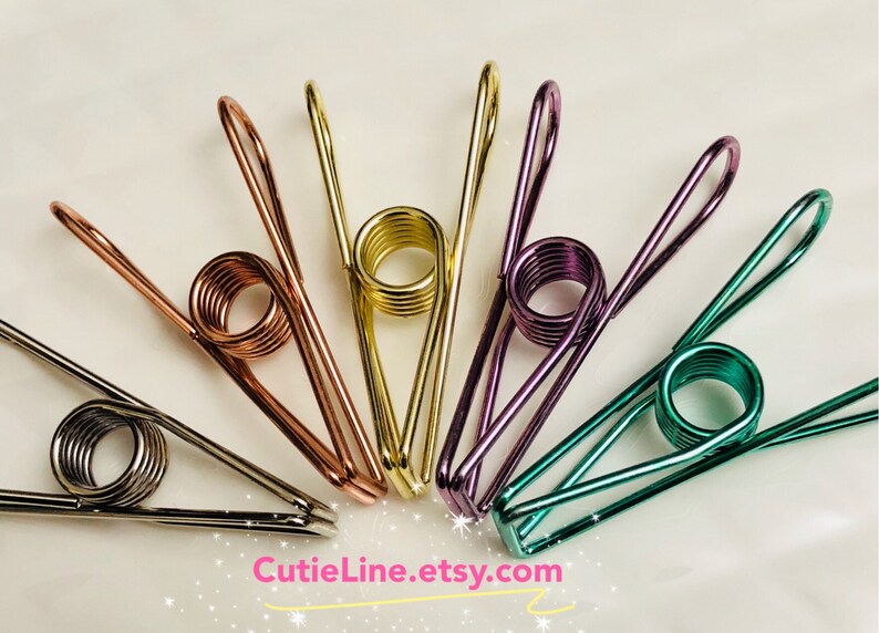 May include: Six metal binder clips in various colors, including copper, gold, purple, and green. The clips are arranged in a circle on a white background. CutieLine.etsy.com is printed at the bottom of the image.
