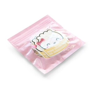 Op de afbeelding: Een roze hersluitbare zak gevuld met witte en gele stickers met een cartoonfiguur met een roze strik. Het figuur zit in een gele mand.