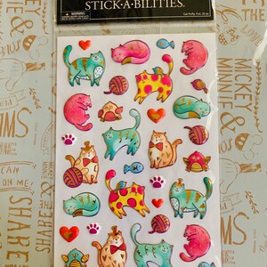 May include: A sheet of 32 colorful, puffy, foil cat stickers. The stickers feature cats in various poses, including sleeping, sitting, and playing with yarn. The stickers are perfect for adding a touch of whimsy to any project.