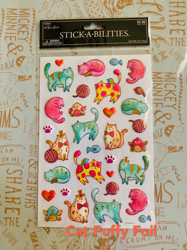 May include: A sheet of 32 colorful, puffy, foil cat stickers. The stickers feature cats in various poses, including sleeping, sitting, and playing with yarn. The stickers are perfect for adding a touch of whimsy to any project.