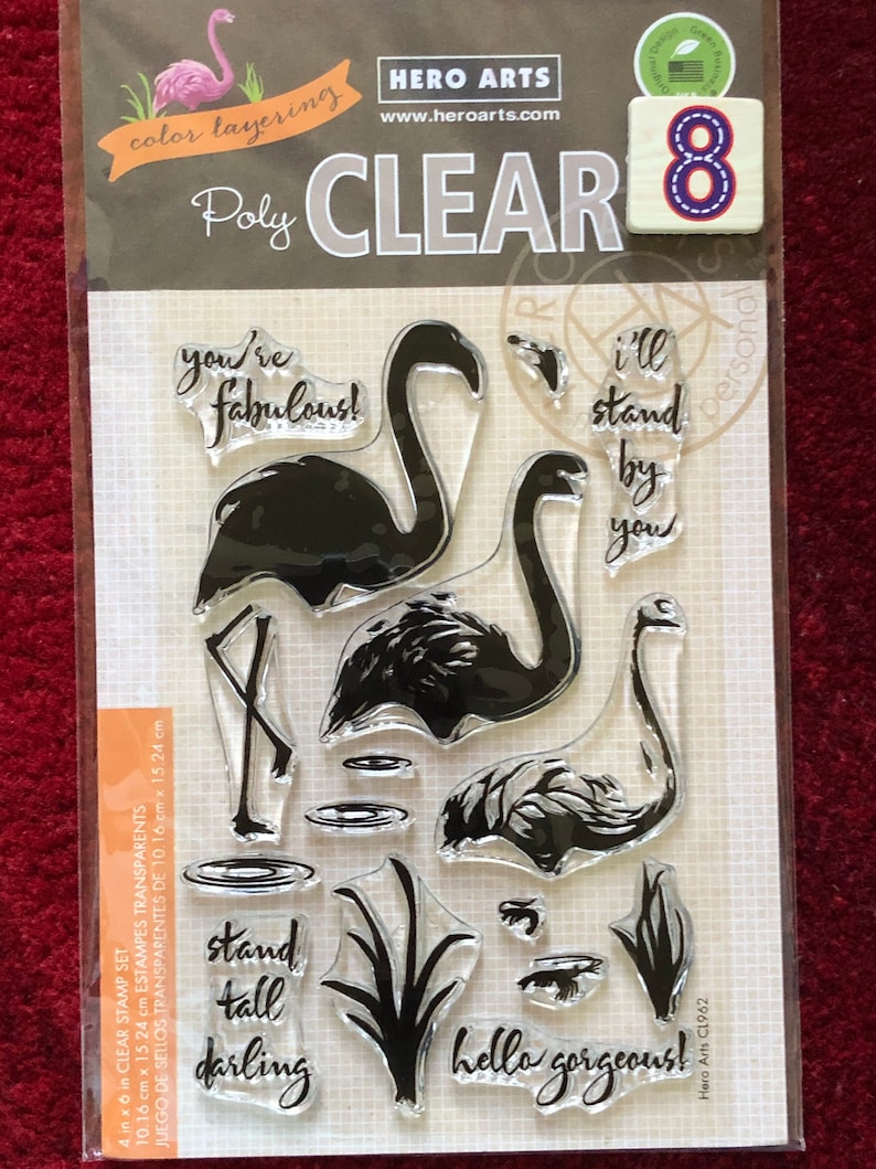 May include: A clear stamp set with 8 stamps featuring flamingo silhouettes, a pond, reeds, and phrases like "you're fabulous!" and "hello gorgeous!" The set is 4 inches by 6 inches (10.16 cm x 15.24 cm).