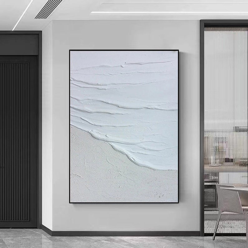 May include: Abstract painting with white and light gray textured brushstrokes, creating a wave-like pattern. The painting is framed in a black frame.