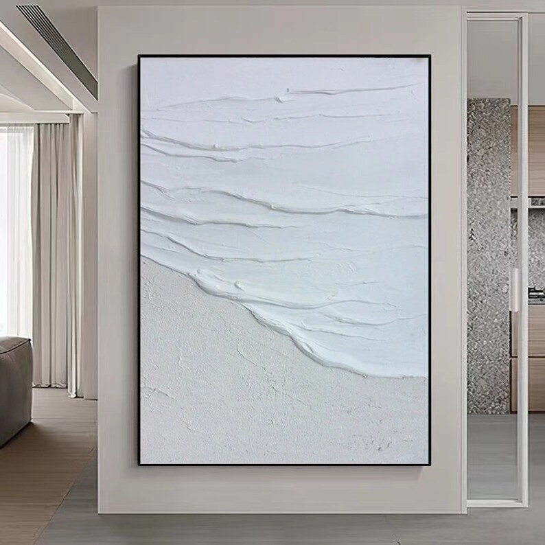 May include: Abstract painting with white textured brushstrokes resembling waves on a beach. The painting has a minimalist style and is framed in black.