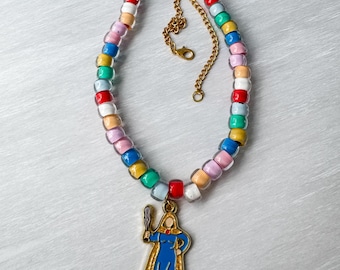 May include: A beaded necklace featuring a gold-tone metal chain extender with a lobster clasp. The necklace is strung with translucent plastic beads in various colors including blue, green, red, white, yellow, and pink, with a central enamel charm.