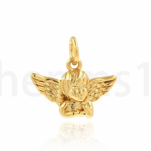 May include: A gold-coloured angel charm pendant with wings and a detailed face. The charm is designed to be worn on a necklace or bracelet.