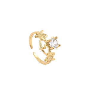 May include: A gold ring with a clear crystal stone set in a bat wing design.