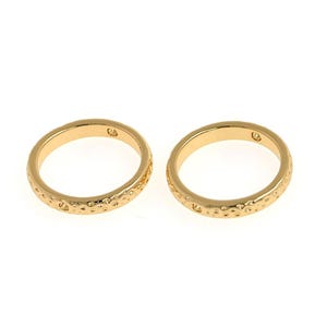 May include: Two gold-colored rings with a textured surface. The rings are simple and elegant.