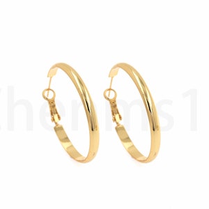 May include: A pair of gold-coloured hoop earrings. The earrings are round with a smooth, polished surface. The clasp is a simple hook and eye closure. The earrings are displayed against a white background.