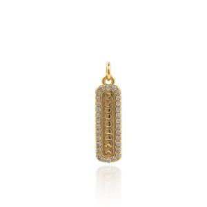 May include: A gold pendant with a rectangular tag featuring a decorative design and a border of small clear stones.