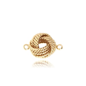 Puede incluir: Un colgante de nudo de color dorado con dos anillos de salto para sujetarlo a un collar o pulsera.