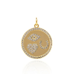 May include: Gold pendant necklace with a round charm featuring a heart, horseshoe, and evil eye design. The charm is encrusted with clear cubic zirconia stones.