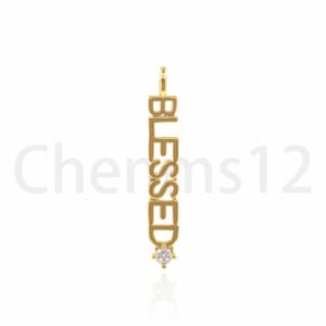 Pode incluir: Encanto de pingente de ouro com a palavra "BLESSED" escrita verticalmente e um pequeno strass transparente na parte inferior.