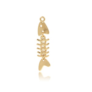 May include: Gold-toned fish bone charm pendant. The charm is made of metal and features a detailed fish bone design with a small fish head at the top.