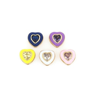 Puede incluir: Cinco abalorios en forma de corazón con esmalte de diferentes colores y un cristal transparente en el centro. Los abalorios son amarillos, blancos, rosas, morados y azules.