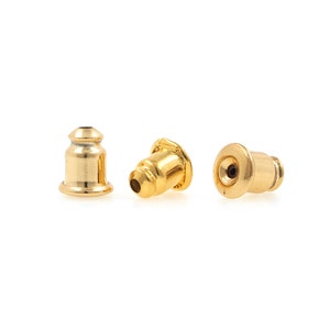 May include: Three gold-colored earring backs. The backs are made of metal and have a smooth, shiny finish.
