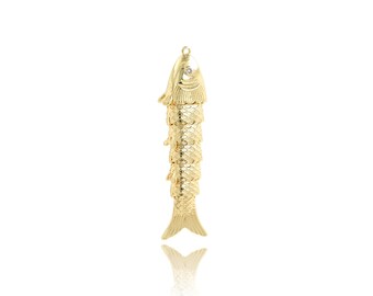 Könnte beinhalten: Goldfarbener Anhänger in Fischform mit einem kleinen, klaren Edelstein auf dem Kopf. Der Anhänger hat detaillierte Schuppen und Flossen sowie eine Schlaufe zum Aufhängen. Das Design ist eine stilisierte Darstellung eines Fisches.