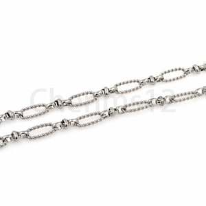 Puede incluir: Un collar de cadena de plata con un diseño de cuerda trenzada y eslabones ovalados. La cadena está hecha de metal y tiene un acabado pulido.