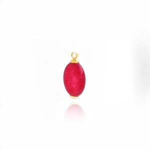 May include: A vibrant red oval gemstone pendant with gold-colored accents. The pendant has a loop at the top for hanging and a gold cap at the bottom. The gemstone is smooth and polished, reflecting light.