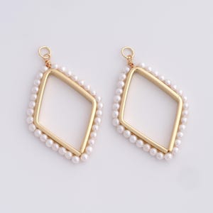 May include: Two gold-colored, diamond-shaped earring pendants. Each pendant features a gold frame with a border of small, white pearls. The top of each earring has a small gold loop for attachment.