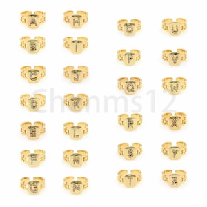 Op de afbeelding: Set van 26 gouden ringen met een vierkant ontwerp. Elke ring heeft een andere letter van het alfabet, versierd met heldere zirkonia-stenen.
