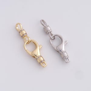 May include: Two metal lobster claw clasps. One is gold-toned, the other is silver-toned. Both clasps have a swivel feature and are embellished with small, clear crystals. The clasps are designed for jewelry making.