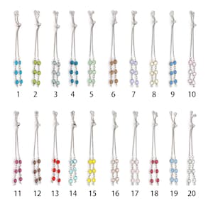 Pode incluir: Vinte pulseiras ajustáveis com correntes prateadas e contas de cristal em várias cores, numeradas de 1 a 20.