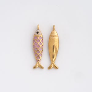 May include: Two gold-colored fish pendants. One pendant features a pink scale pattern and a black eye, while the other is solid gold. Both have a loop at the top for hanging and small fins at the bottom. These pendants are ideal for jewelry making.