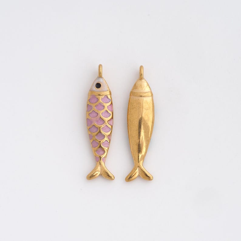 May include: Two gold-colored fish pendants. One pendant features a pink scale pattern and a black eye, while the other is solid gold. Both have a loop at the top for hanging and small fins at the bottom. These pendants are ideal for jewelry making.