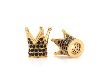 May include: Two gold-colored crown-shaped beads with black gemstones. The beads have a detailed design with pointed tips and a cylindrical base. The gemstones are set in a pattern around the crown.