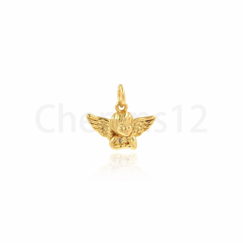 May include: A gold-coloured angel charm pendant with wings and a detailed face. The charm is designed to be worn on a necklace or bracelet.